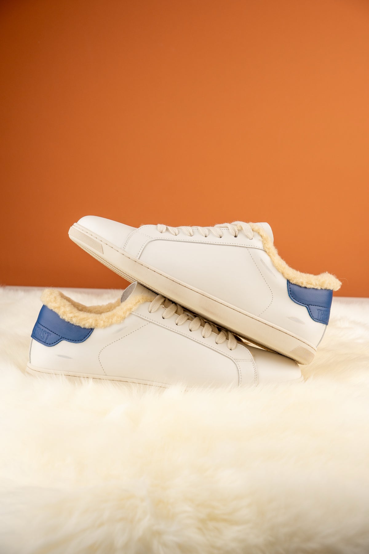 Geneva Wool Navy Heel Unsigned, pair stacked on sheepskin against an orange backdrop