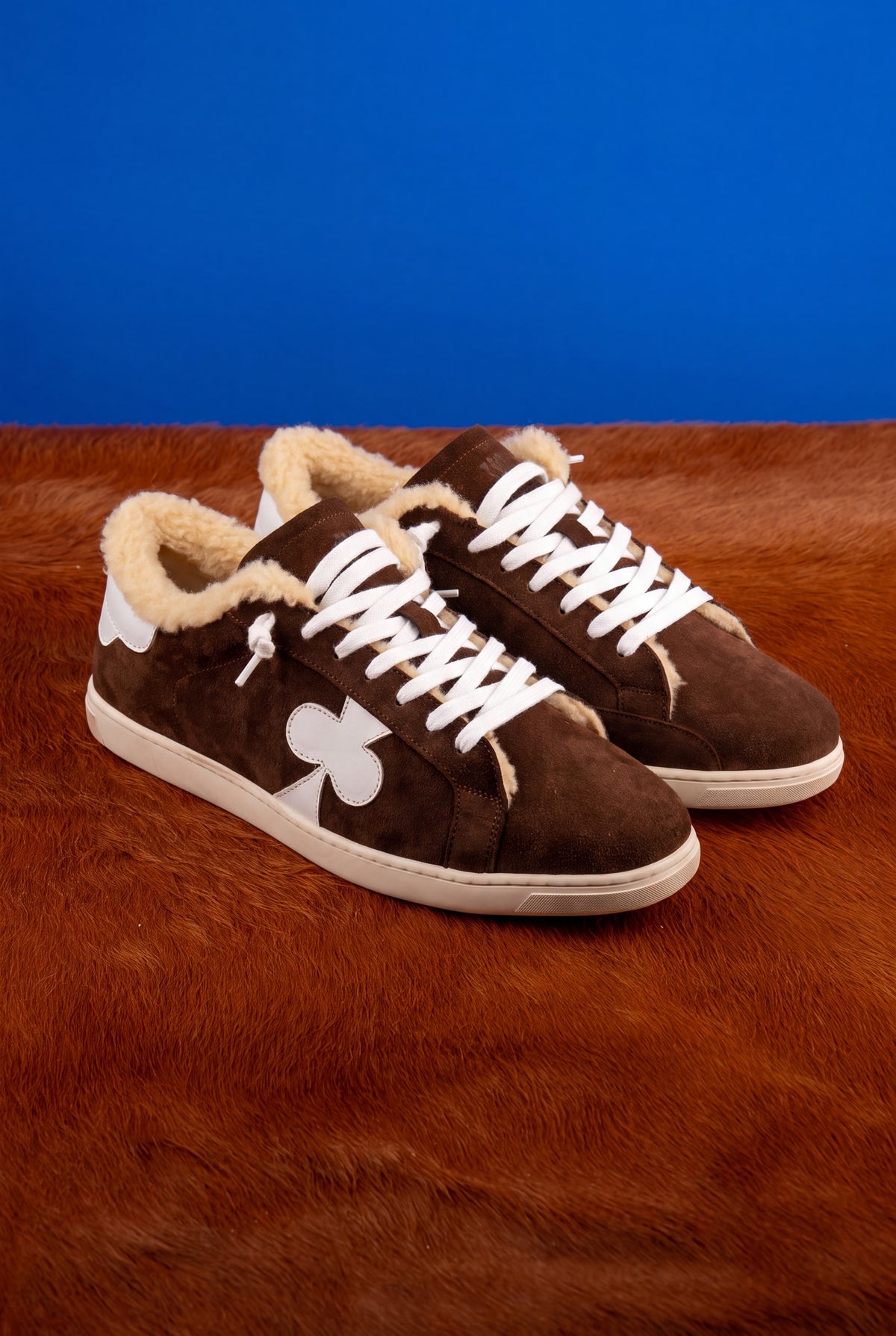 Geneva Wool Chocolate Suede, pair on cowhide against a blue backdrop